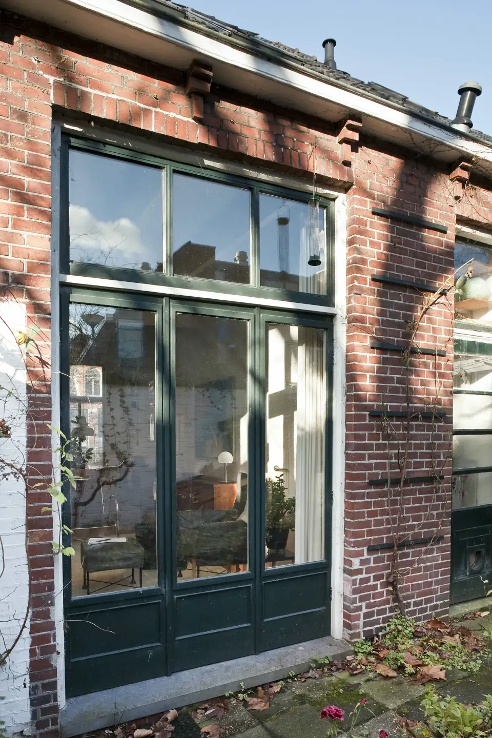 Een donkergroen geschilderd houten kozijn met deuren en bovenlichten in een bakstenen achtergevel in Groningen
