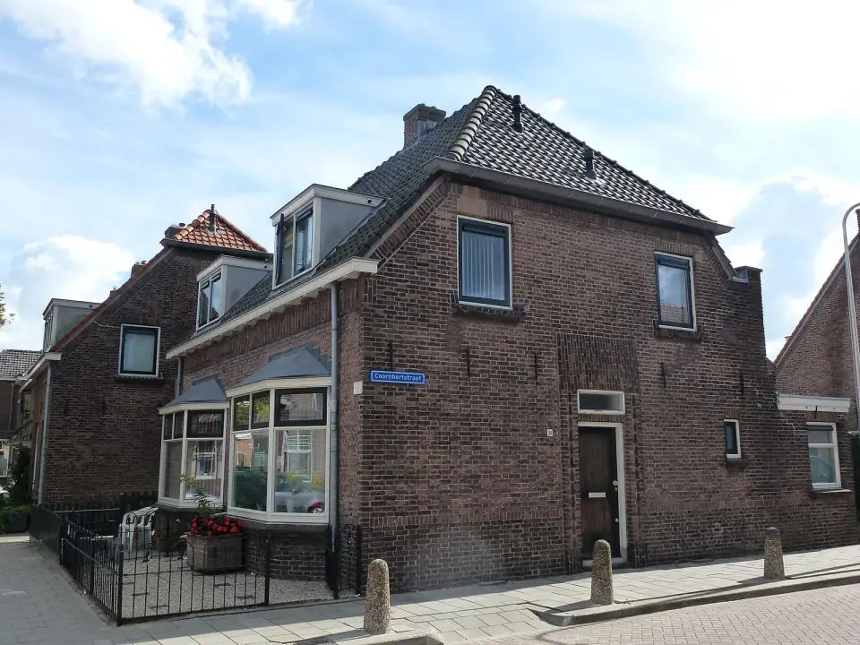 Een bakstenen hoekhuis met een erker en kozijnen in wit en donkergroen aan een Nederlandse straat