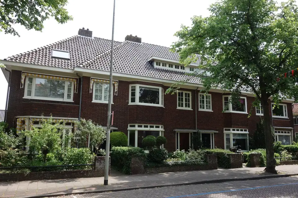 Een rij jaren-dertigwoningen van rode baksteen met witte houten kozijnen, erkers en voortuinen aan een straat in Hoorn