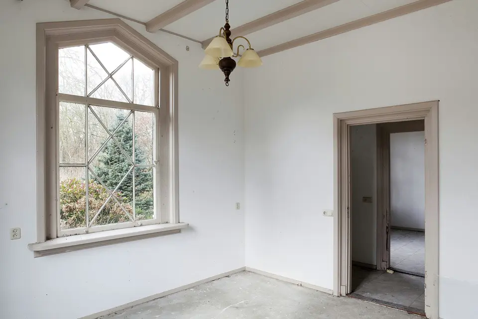 Een lege kamer in een oud huis in Nijkerk met een hoog houten raam met ruitvormige roeden, van binnen gezien